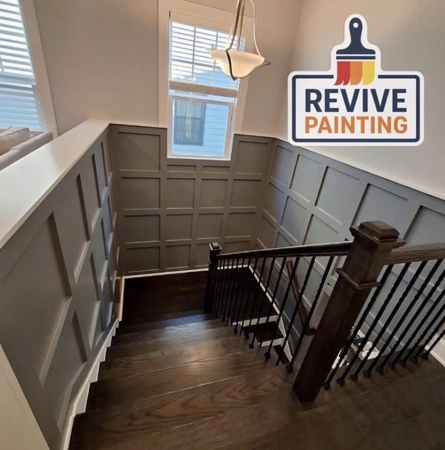 A stairwell with gray board-and-batten wainscoting and a dark wood rail