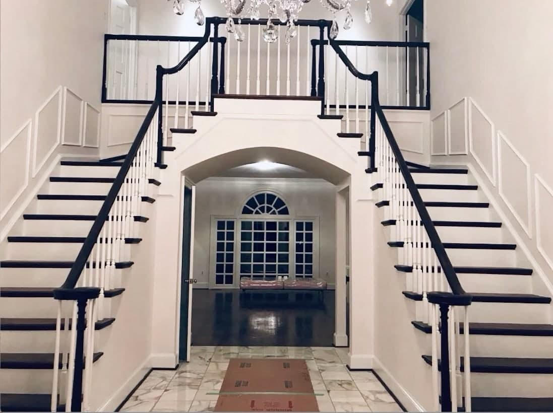 A two-story foyer with a double staircase painted white with black handrails